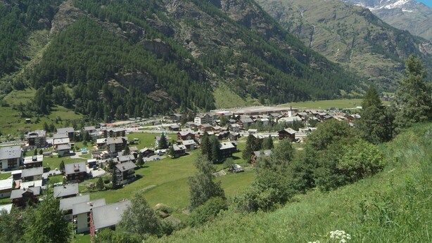 A mountain village with traditional buildings, a central square, and a backdrop of snow-capped peaks. - Nice apartment for 4 people with WIFI, TV and balcony (Zermatt)