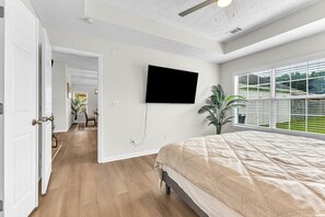 Een slaapkamer met een groot bed, een flatscreen-tv aan de muur en een raam met zonwering.