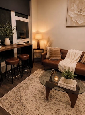 Un salon chaleureux avec un canapé en cuir marron, une table basse en verre et un tapis à motifs.