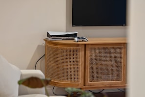 A room with a wooden cabinet, a flat-screen TV mounted on the wall, and a gaming console on top of the cabinet. - Hallia House – Coastal Retreat (Readhead)