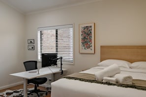 A bedroom with a bed, a desk with a computer, a chair, and a window with blinds. - Hallia House – Coastal Retreat (Readhead)