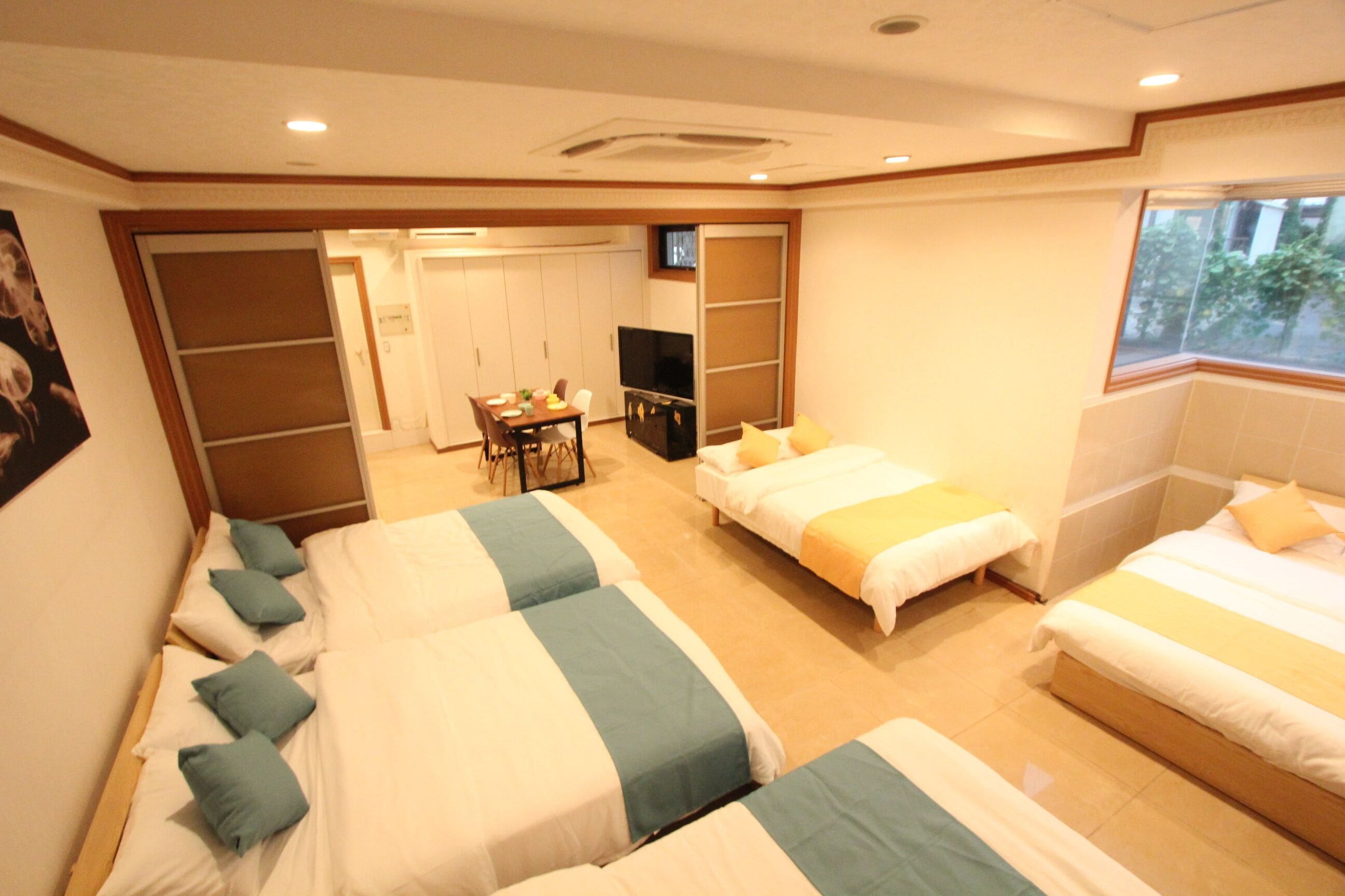 A hotel room with three beds, a television, and a dining area.