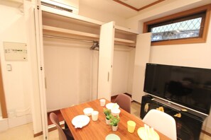 A compact living space with a wooden dining table set for four, a television, and a sliding door closet. - Spacious Private Stay Near Higashi-Shinjuku | Sleeps 10 | Families & Groups | WiFi (1) (新宿区新宿７丁目)