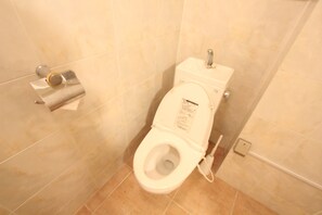 A standard hotel bathroom with a toilet, a paper towel dispenser, and a flush handle. - Spacious Private Stay Near Higashi-Shinjuku | Sleeps 10 | Families & Groups | WiFi (1) (新宿区新宿７丁目)