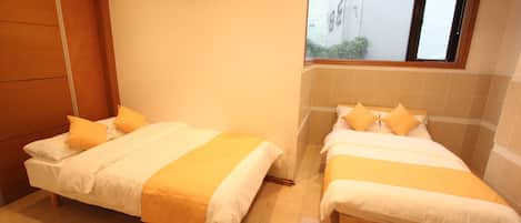 Habitación de hotel con dos camas, cada una con ropa de cama blanca y amarilla, y un ventanal con vista al exterior.