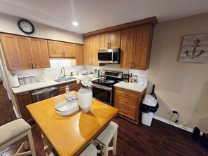 A compact kitchen with wooden cabinets, a microwave, a stove, and a sink. There is a clock on the wall and a sign that says 'Coffee Time'.