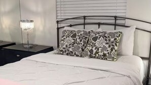 Una cama con edredón blanco, manta rosa y almohadas estampadas.