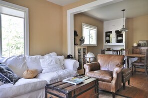 Ein Wohnzimmer mit einem weißen Sofa, einem Ledersessel, einem Holztisch mit einer Zeitschrift und einem Globus.