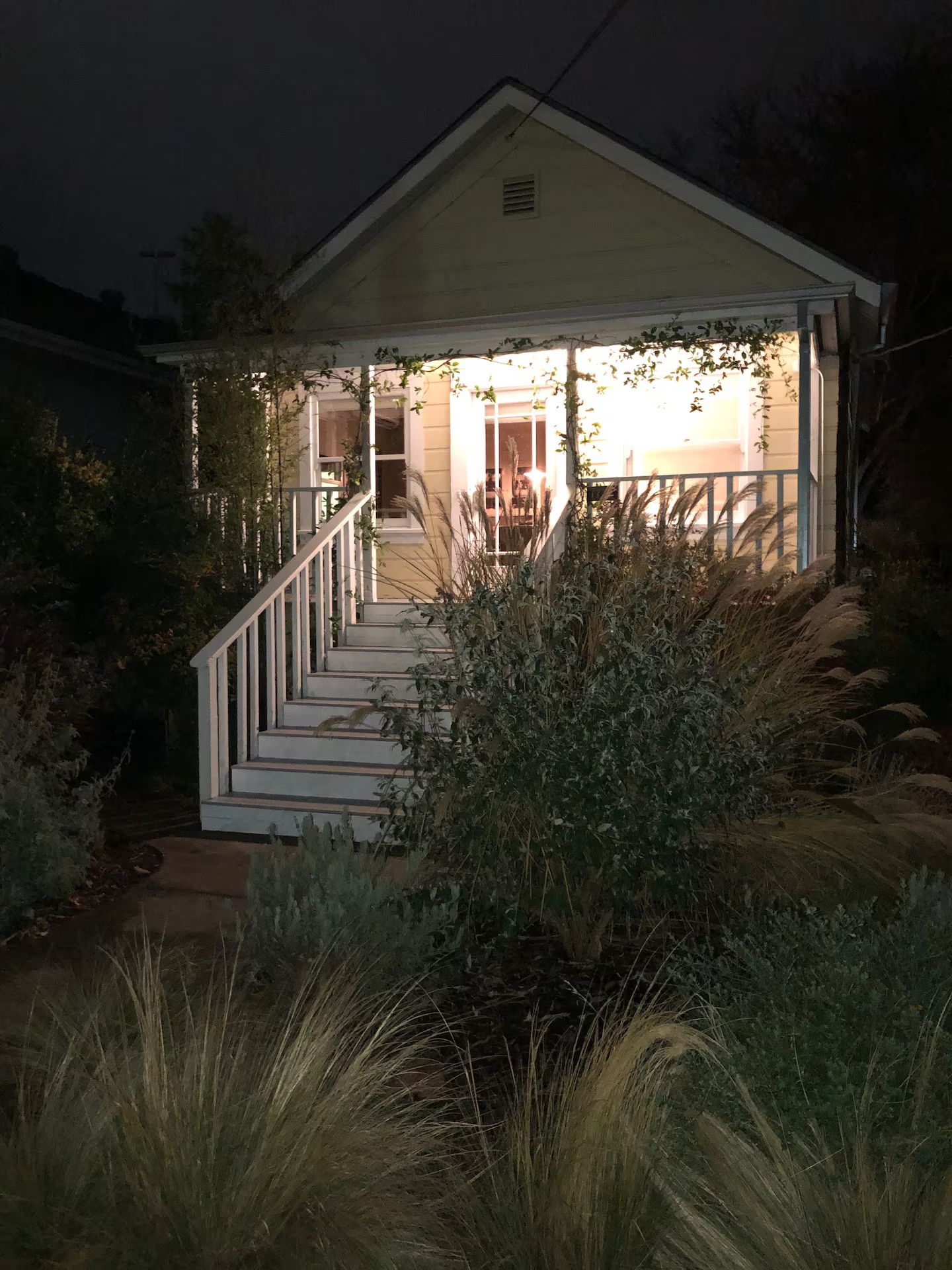A house with a porch, a staircase leading to the entrance, and surrounding vegetation.