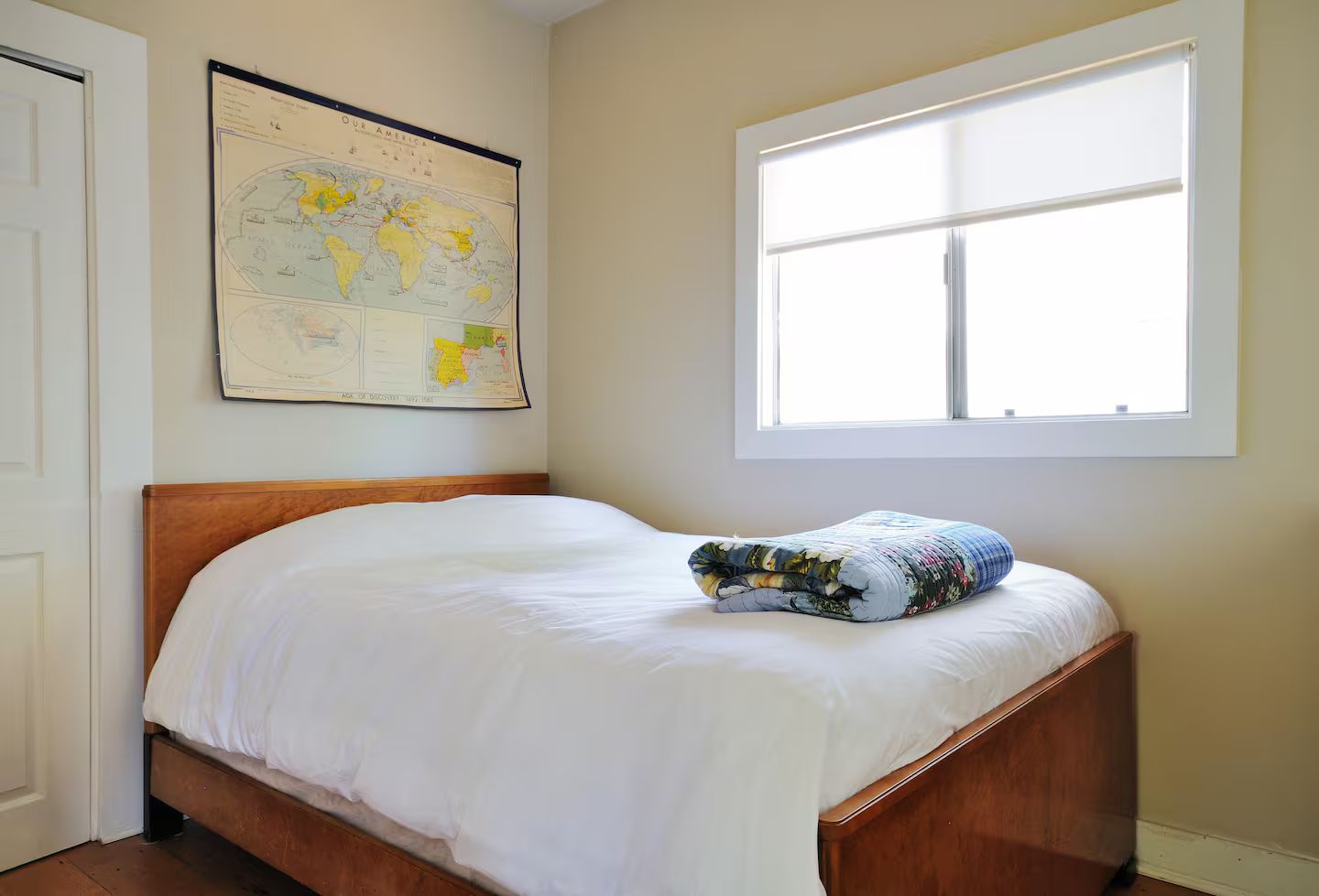 A bedroom with a wooden bed, a large window, and a world map on the wall.