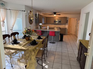 A dining area with a table set for four, a kitchen with modern appliances, and a ceiling fan. - 3-bedroom house in superb Alexander with cool AC (Alexander)