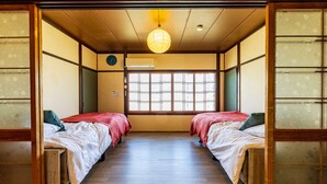 Ein traditioneller japanischer Raum mit zwei Betten, einem Holzboden, einem Shoji-Bildschirm, einer hängenden Papierlaterne und einer Uhr an der Wand.
