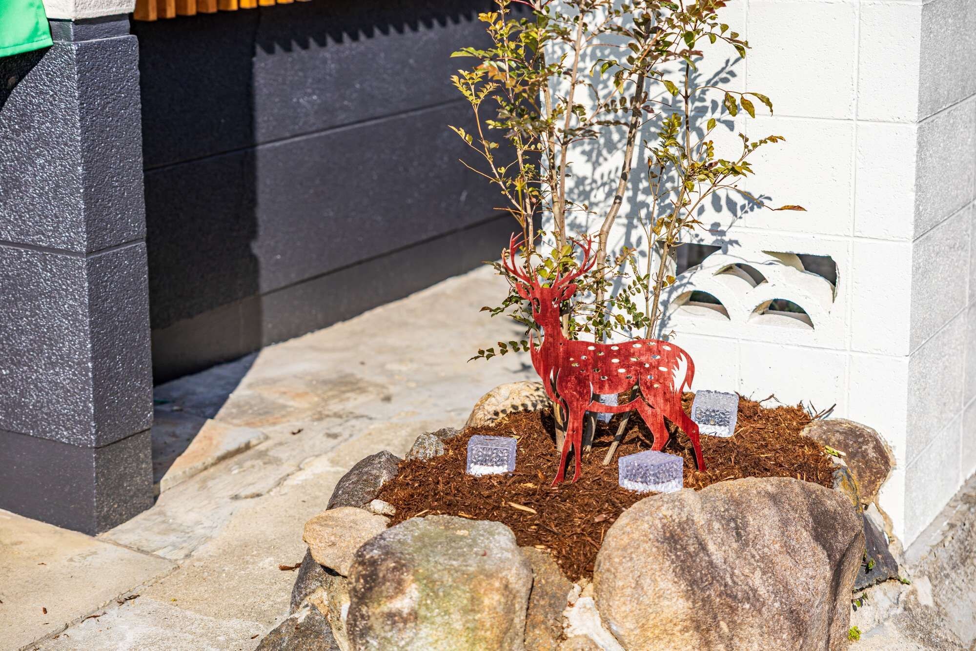 A garden area with a decorative red deer sculpture, rocks, and a small tree.