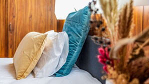 Ein Bett mit drei Kissen in verschiedenen Farben und einer Vase mit getrockneten Blumen.