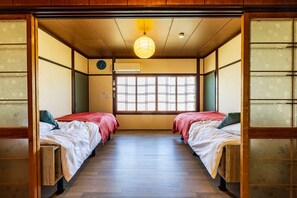 A traditional Japanese room with two beds, a wooden floor, a shoji screen, a hanging paper lantern, and a clock on the wall.