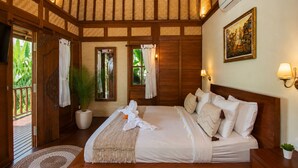 A bedroom with a large bed, wooden beams, a potted plant, and a painting on the wall. - Ubud 1BR Villa Resort Wooden Nakula (Ubud)