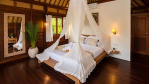 A bedroom with a canopy bed, a large mirror, a potted plant, and a nightstand with a lamp. - Ubud 1BR Villa Resort Wooden Nakula (Ubud)
