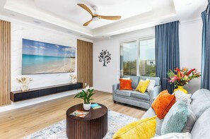 Un salon moderne doté d’un grand téléviseur à écran plat, d’un ventilateur de plafond et d’un canapé agrémenté de coussins aux couleurs vives.