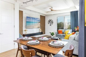 A dining area with a wooden table set for four, a ceiling fan, and a large window with a view of the outdoors. - Dreamz Retreat Villa your tropical escape (Cooper Jack Bay Settlement)