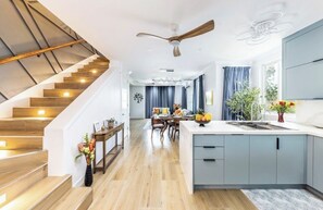 Une cuisine moderne dotée d’un îlot central, d’un escalier en bois et d’un coin repas offrant une vue sur le salon.