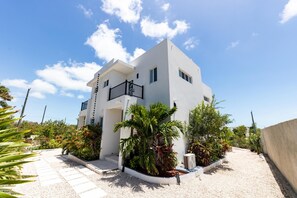 A modern two-story building with a white facade, a balcony with black railings, and a gravel driveway. - Dreamz Retreat Villa your tropical escape (Cooper Jack Bay Settlement)