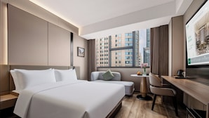 A hotel room with a large bed, a desk, a chair, and a view of the cityscape. - Madison Hotel (Guangzhou)