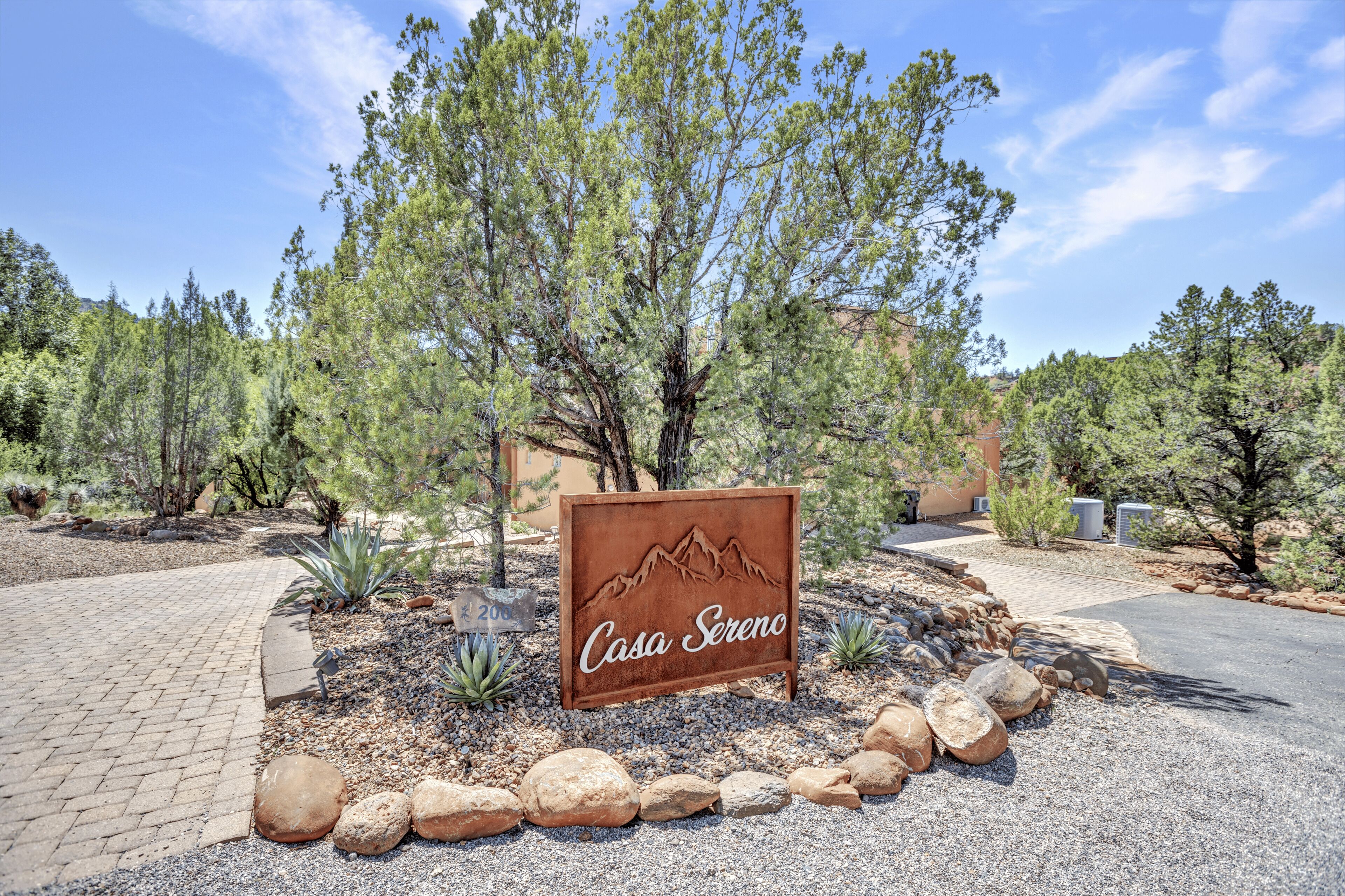 A sign with 'Casa Sereno' and a mountain design, surrounded by trees and rocks.
