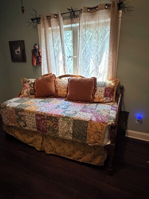 A bed with a quilt, a window with curtains, a wall-mounted lamp, and a picture frame.
