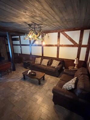 Een gezellige woonkamer met een houten plafond, een bruine zithoek, een salontafel en een kroonluchter.