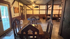 Zona de menjador amb taula i cadires de fusta, un penjallum i una llar de pedra.