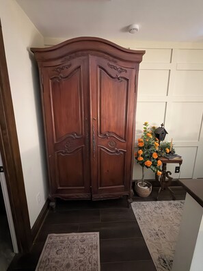 Ein hölzerner Kleiderschrank mit aufwendigen Schnitzereien, ein kleiner Tisch mit einem Blumentopf und ein gemustertes Teppich auf Fliesen.