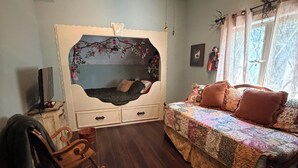 Un dormitori amb llit, una cadira bressol, un aparador i una finestra amb cortines.