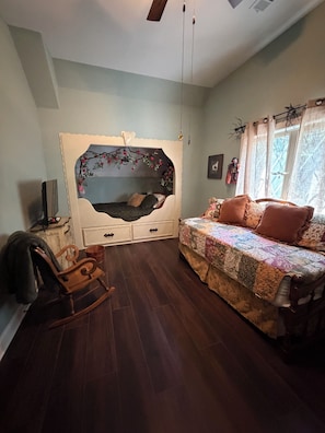 Une chambre à coucher avec un lit, un fauteuil à bascule, une commode et une fenêtre avec des rideaux.