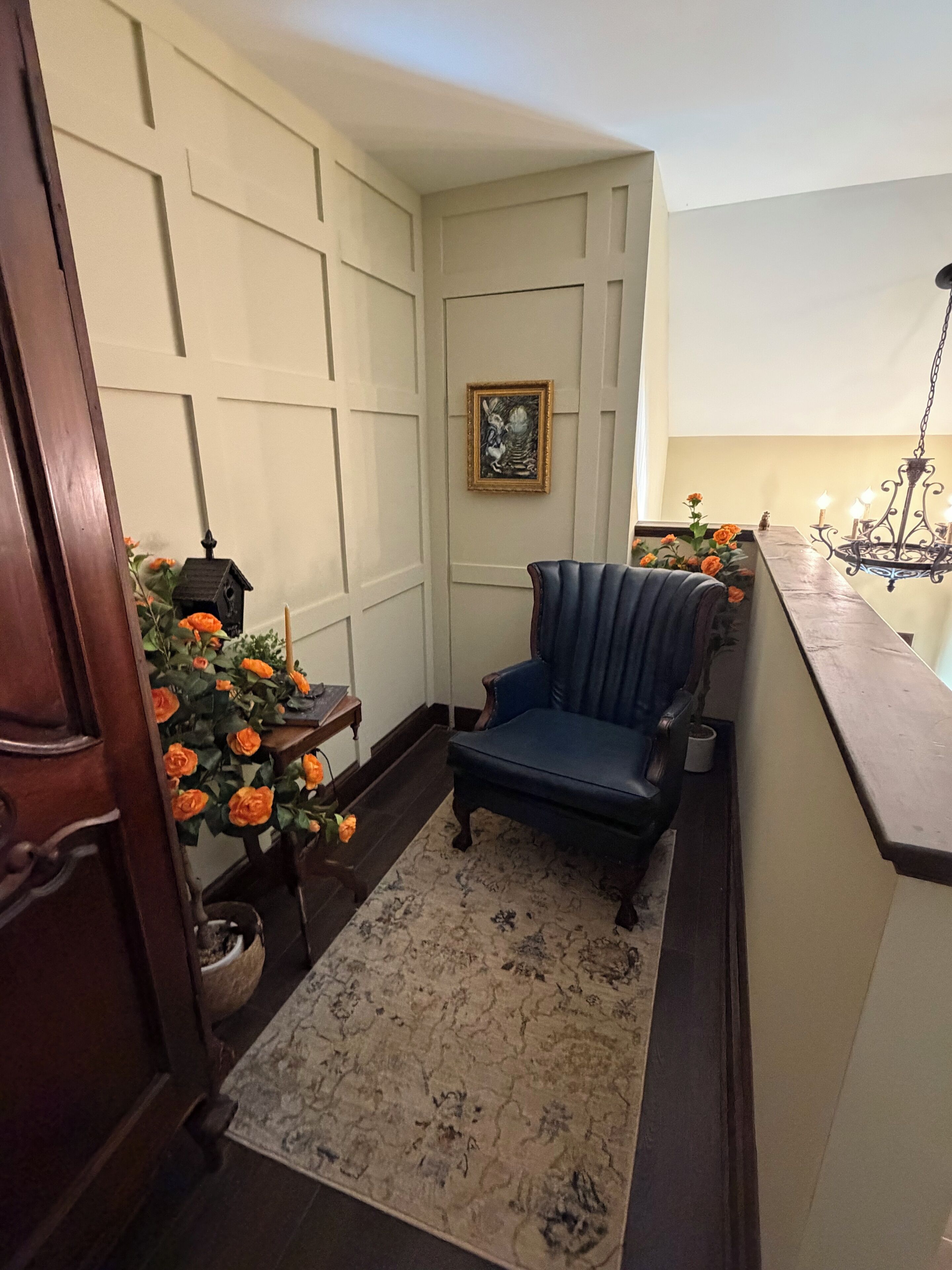 Una habitación de esquina con un sillón azul, una mesita con un farolillo y una planta en maceta con flores anaranjadas.