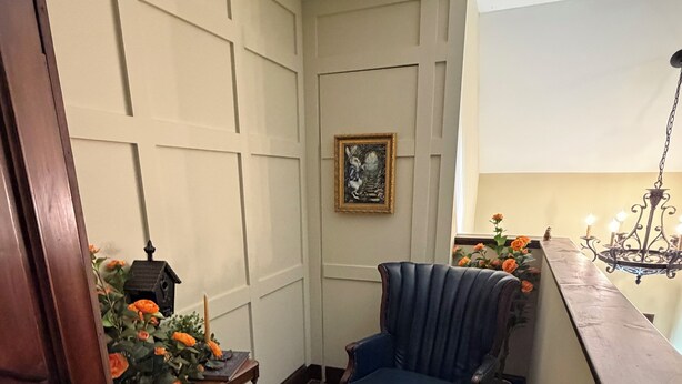A corner room with a blue armchair, a small table with a lantern, and a potted plant with orange flowers.