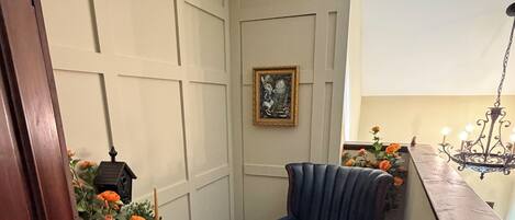 Una habitación de esquina con un sillón azul, una mesita con un farolillo y una planta en maceta con flores anaranjadas.