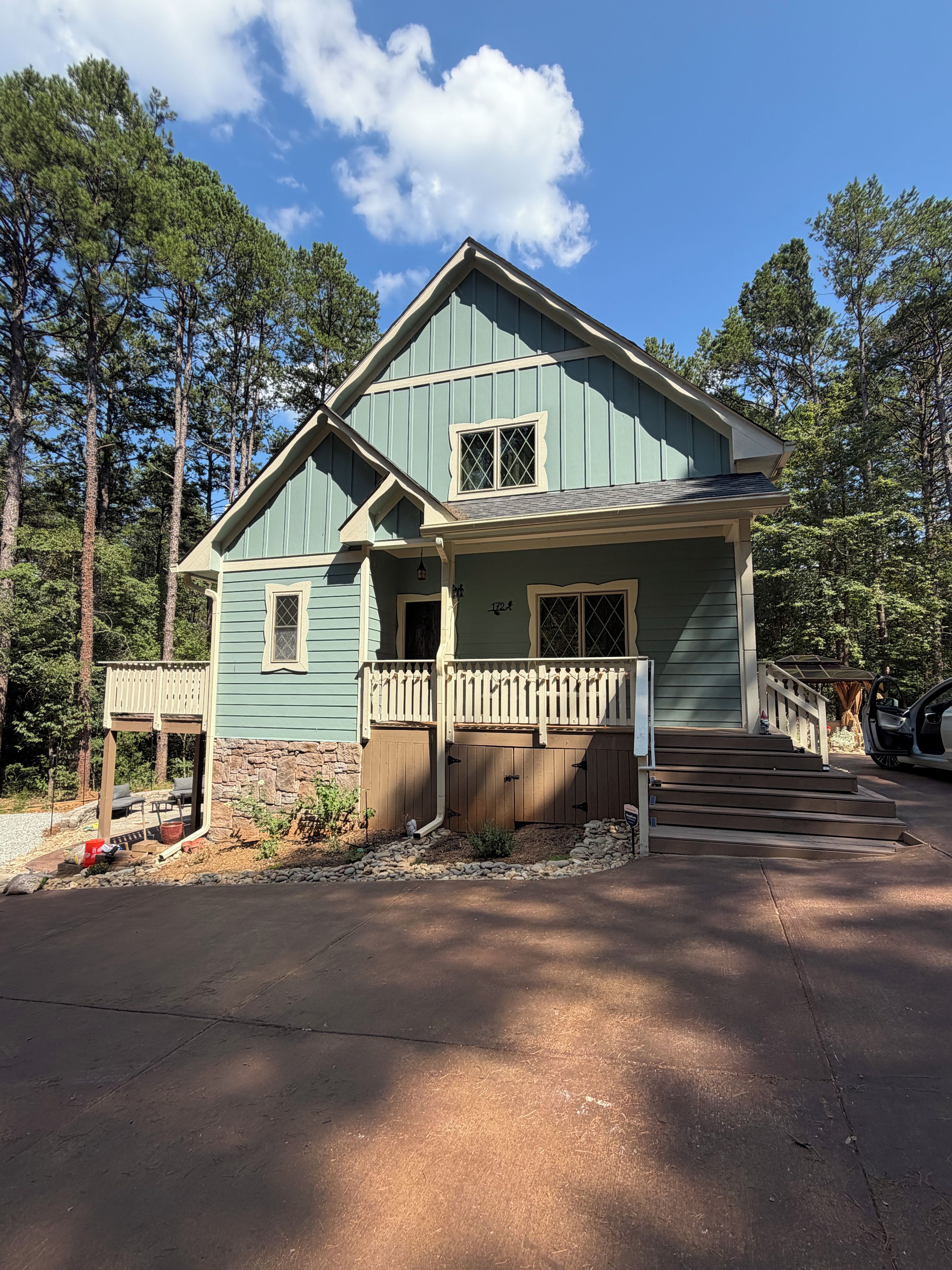 A two-story house with a porch, a stone foundation, and a driveway leading to a parked car.