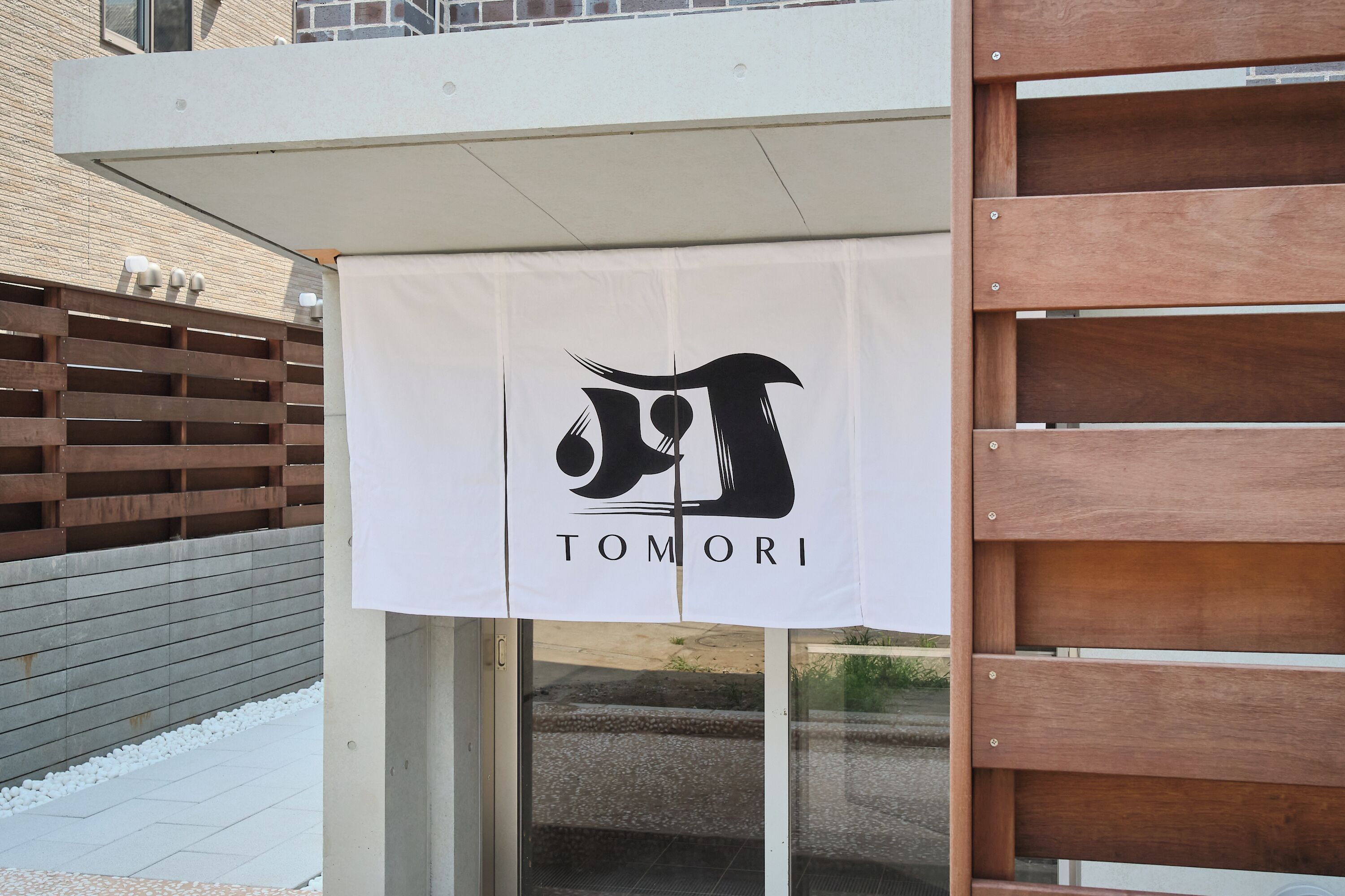 Entrada de um prédio com uma faixa branca exibindo um logotipo e a palavra 'TOMORI'.