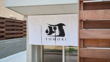 Entrada de um prédio com uma faixa branca exibindo um logotipo e a palavra 'TOMORI'.