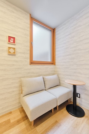 A room with a sofa, a small round table, and a window with a wooden frame. - Tomori (Tokyo)