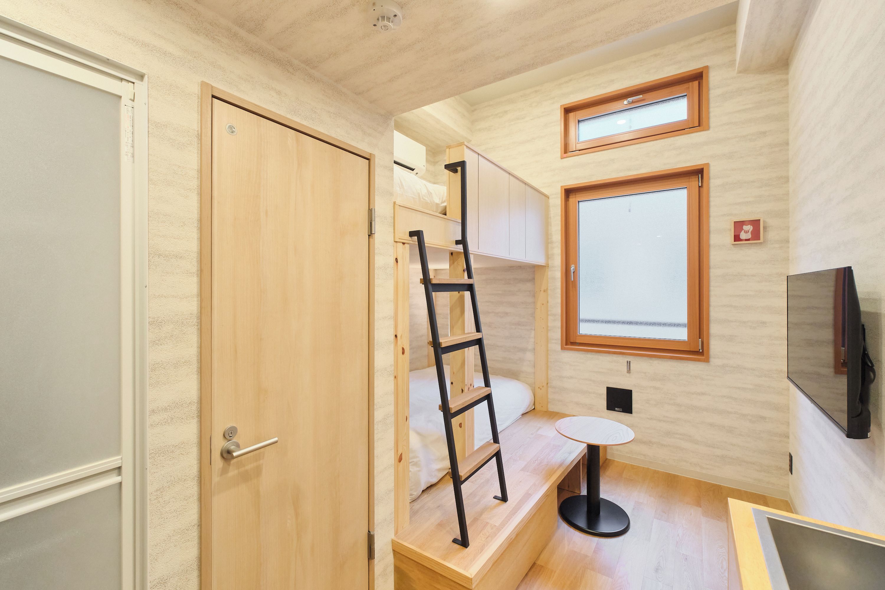 A compact room with a wooden door, a ladder, a small table, a bed, and a television.