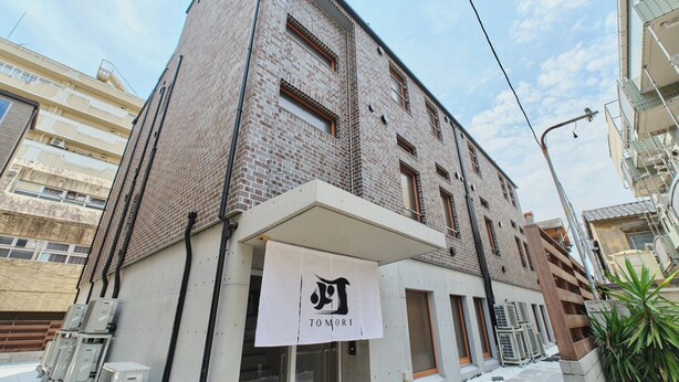 Um edifício de vários andares com fachada de tijolos, uma cobertura branca com um logotipo e aparelhos de ar condicionado no nível da rua.