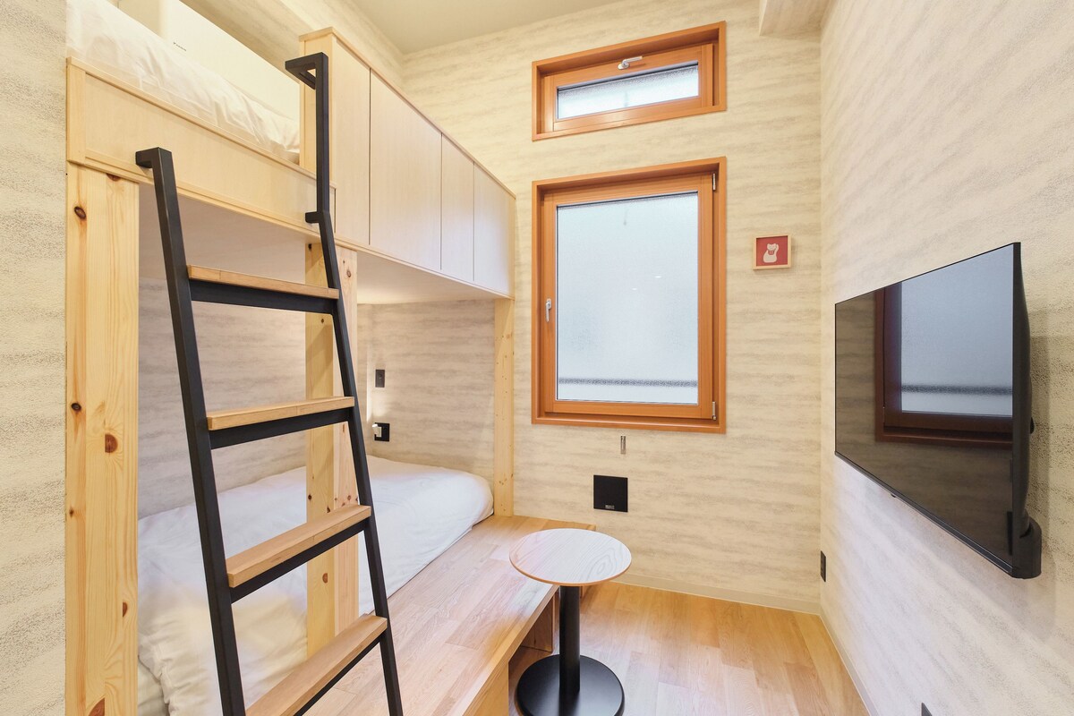 A compact room with bunk beds, a small round table, a TV, and a window.