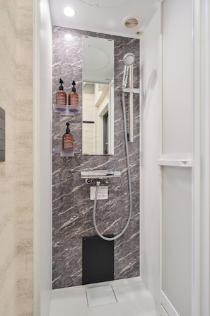 A modern bathroom with a marble wall, a built-in mirror, a handheld showerhead, and a toilet paper holder. - Tomori (Shinjuku-ku)