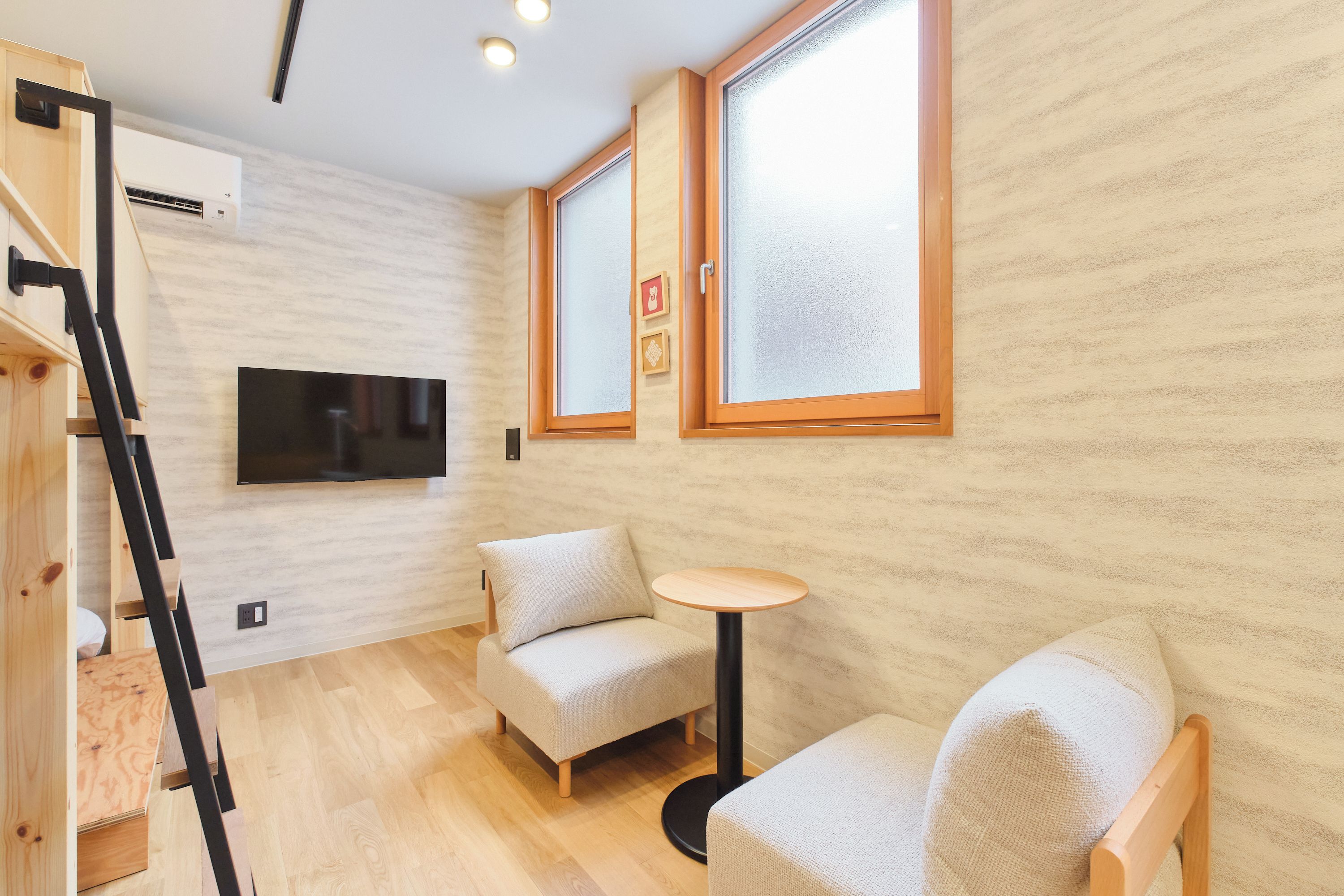 A room with a wooden floor, a sofa, a small round table, and a TV mounted on the wall.