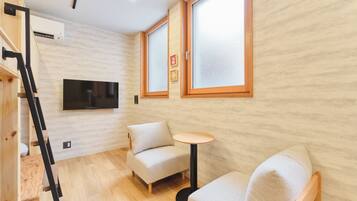 A room with a wooden floor, a sofa, a small round table, and a TV mounted on the wall.