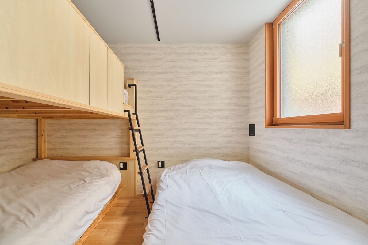 A small, compact room with bunk beds, a ladder, a window, and a wall-mounted light fixture.