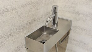 Uma pia de casa de banho em aço inoxidável com uma torneira de comando único e mangueira flexível.