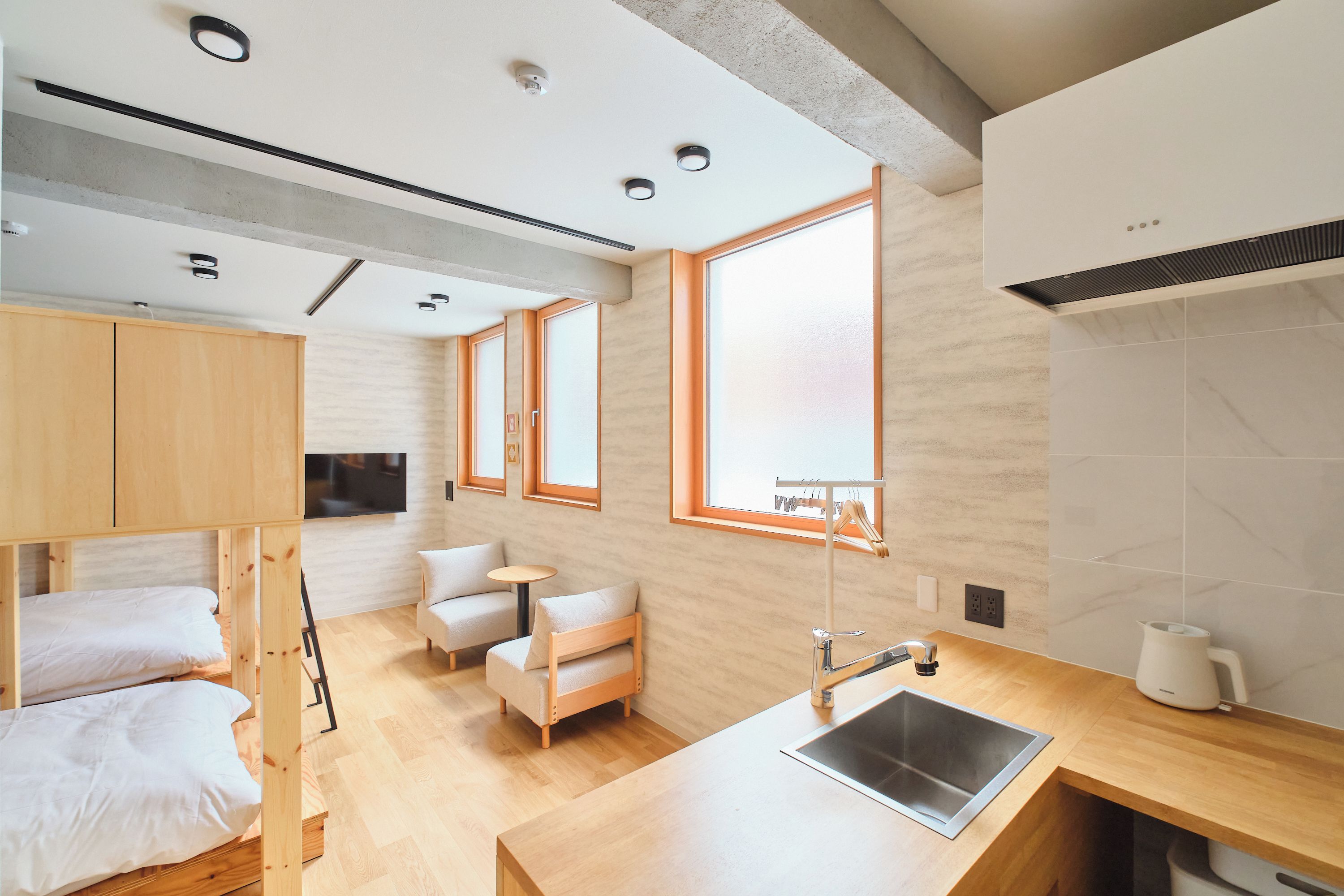 A modern, compact room with bunk beds, a small seating area, a sink, and a window providing natural light.