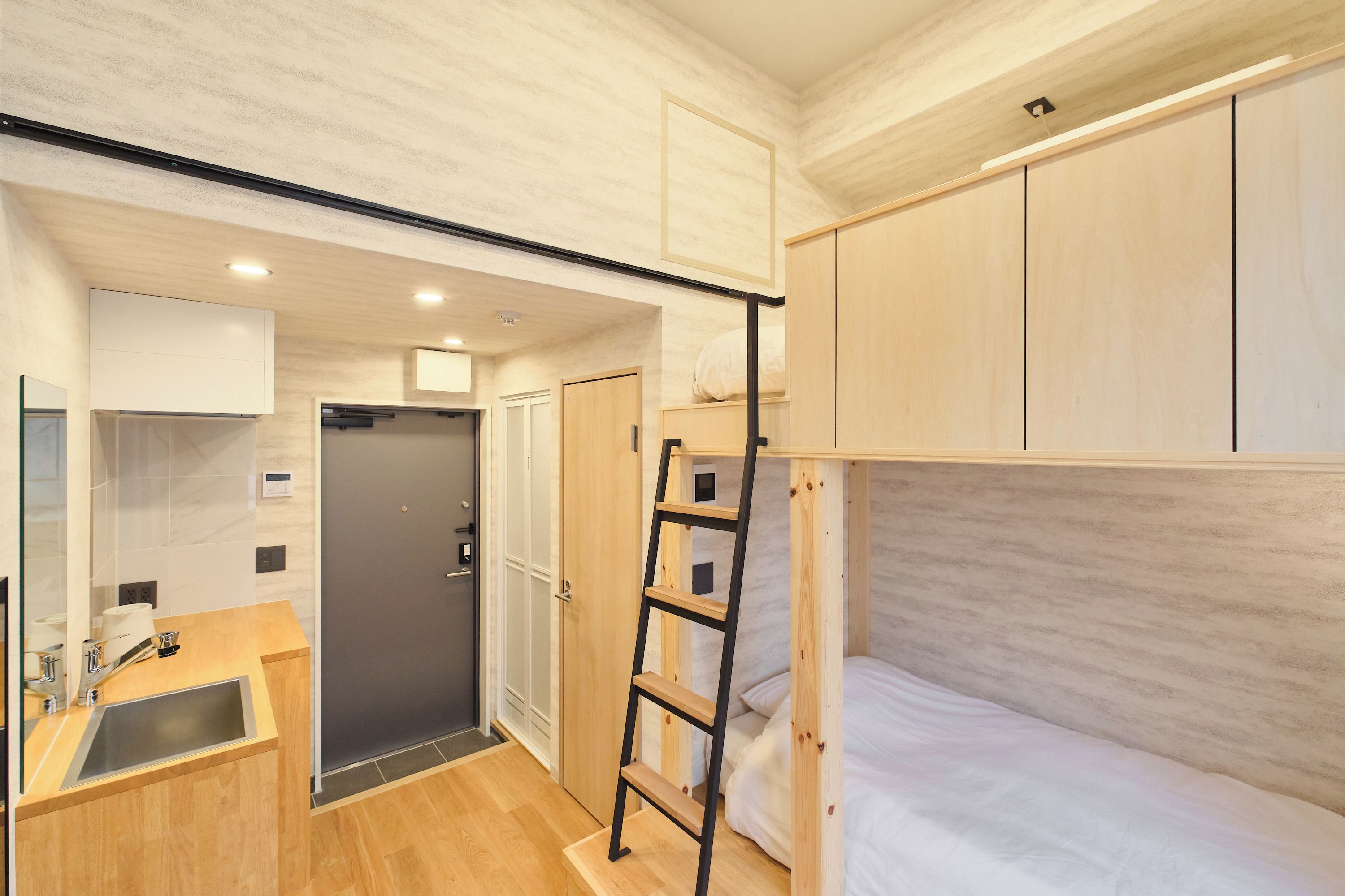 A compact room with a bunk bed, a small kitchenette, and a shower area.